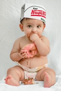 Baby eating a pink frosted donut with chocolate frosting